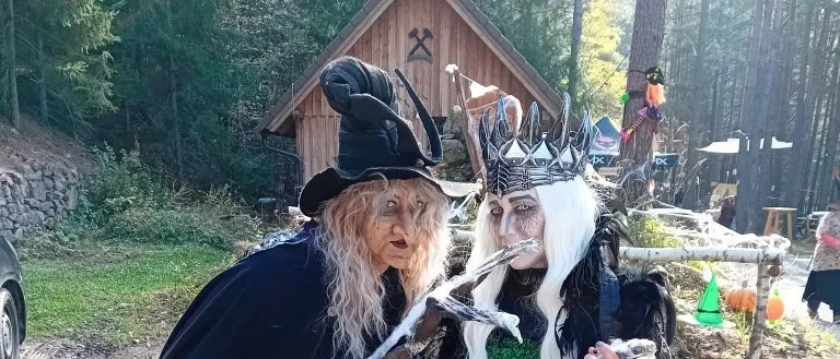 Zwei Menschen in Hexenkostümen stehen vor einem Holzhaus.