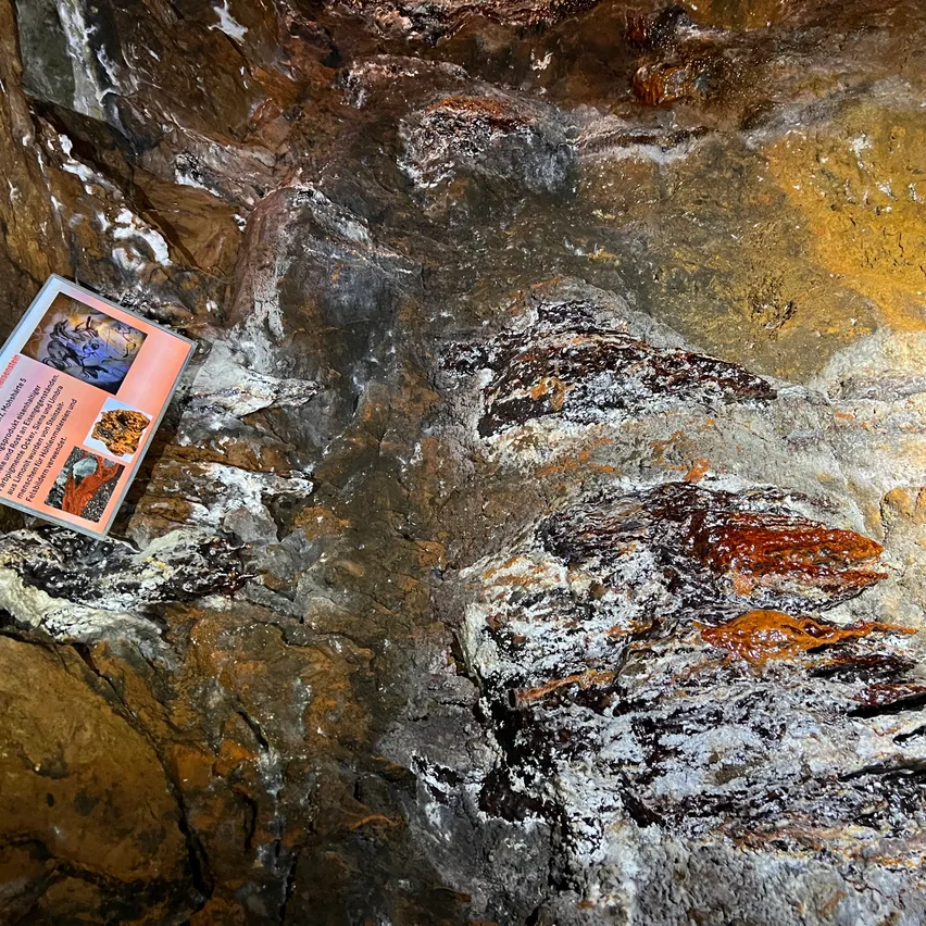 Nahaufnahme einer Felsformation mit einem kleinen Schild auf der linken Seite, das verschiedene Mineralien und ihre Eigenschaften darstellt.