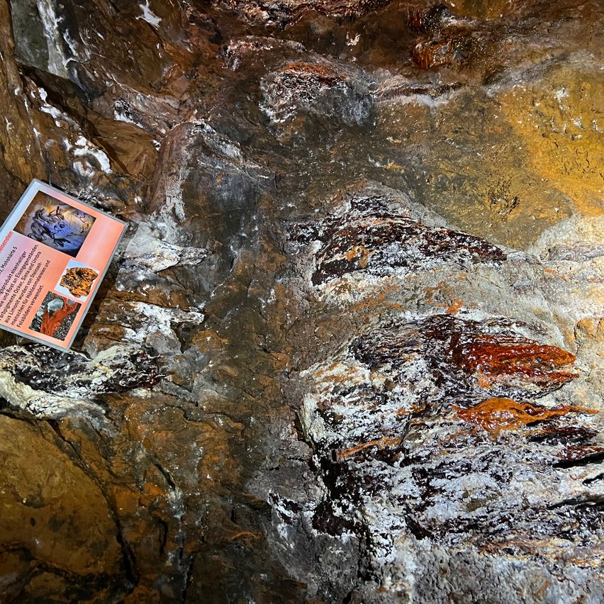 Nahaufnahme einer Felsformation mit einem kleinen Schild auf der linken Seite, das verschiedene Mineralien und ihre Eigenschaften darstellt.