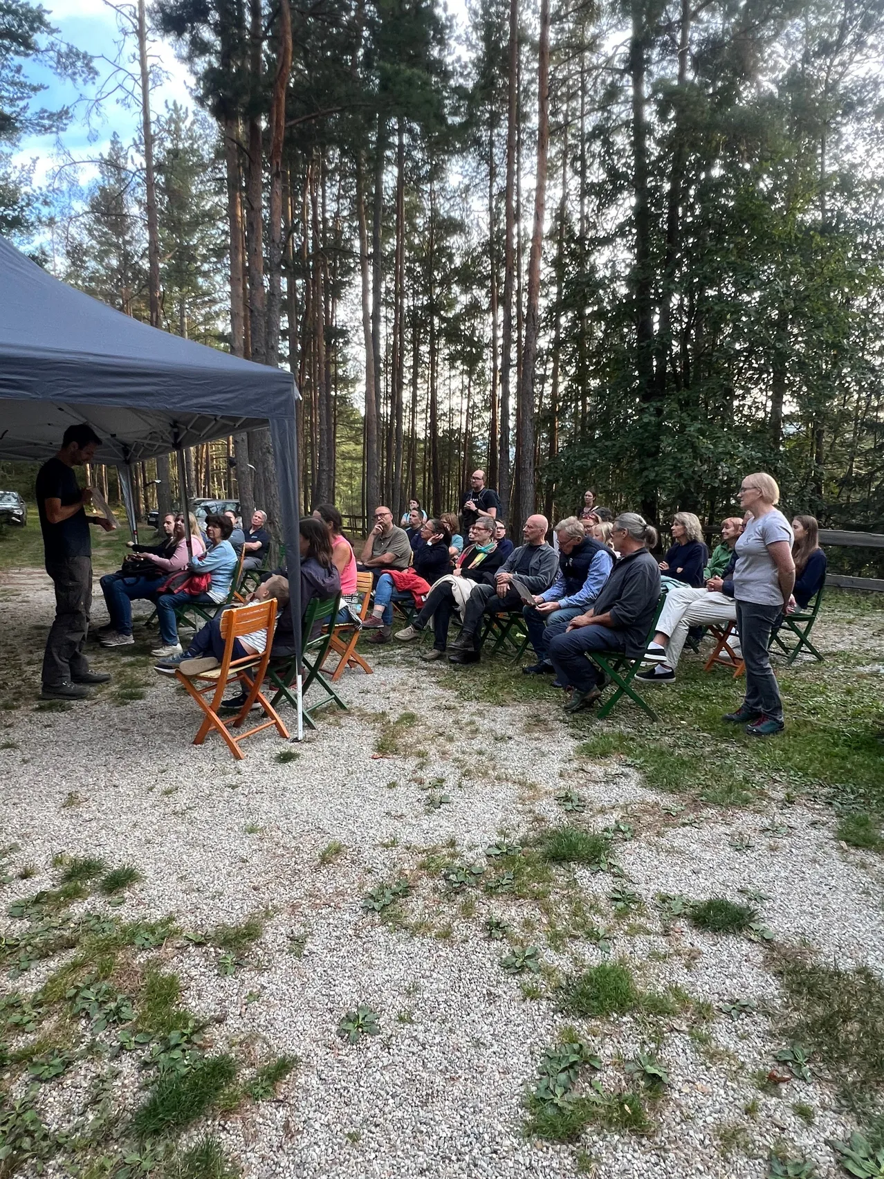 Eine Gruppe von Menschen ist in einem Kreis unter einem Zelt im Wald versammelt.