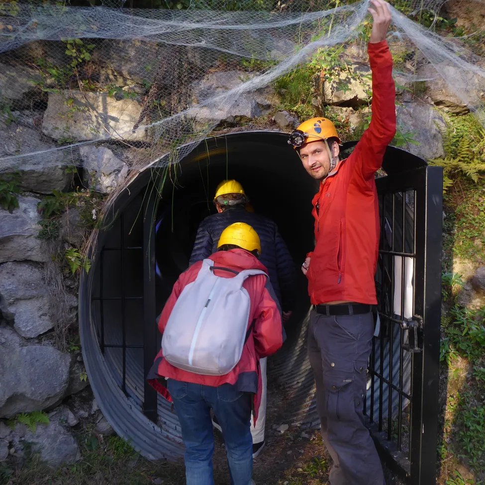 Eine Gruppe von Menschen verlässt einen Tunnel, wobei ein Mann einen roten Mantel und einen Helm trägt.