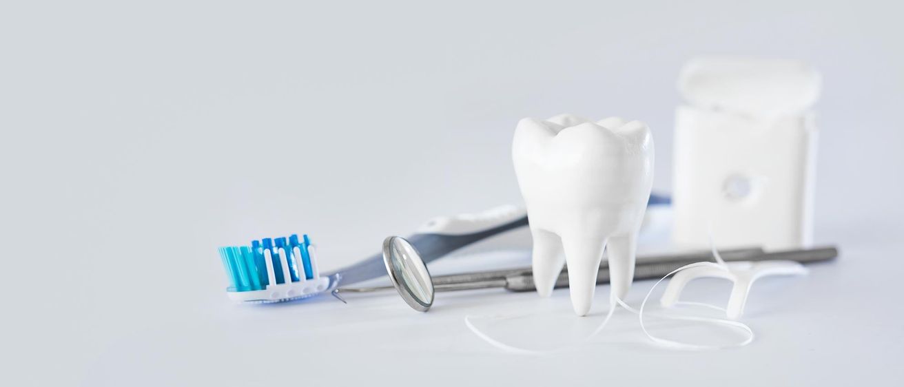 Eine Zahnbürste mit blauen Borsten liegt neben einem Zahnarztspiegel und einem Zahnmodell auf weißem Hintergrund.