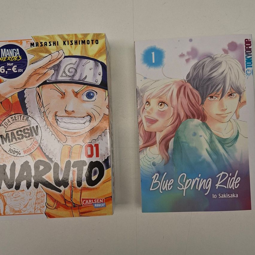 Zwei Manga-Bücher sind auf einer weißen Oberfläche ausgestellt. Das linke Buch ist Naruto und das rechte Buch ist Blue Spring Ride.