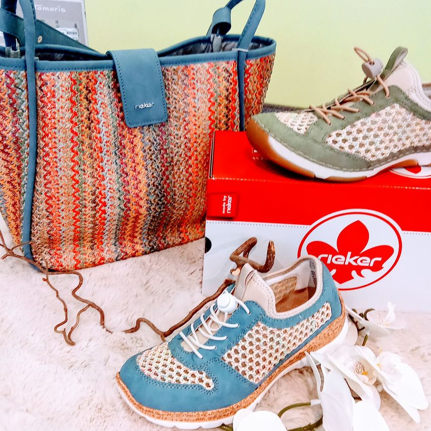 Zwei Rieker-Schuhe, ein blauer und ein grüner, und eine blaue Rieker-Handtasche mit einem kleinen Korb, auf einem roten Kasten und weißem Pelztuch.
