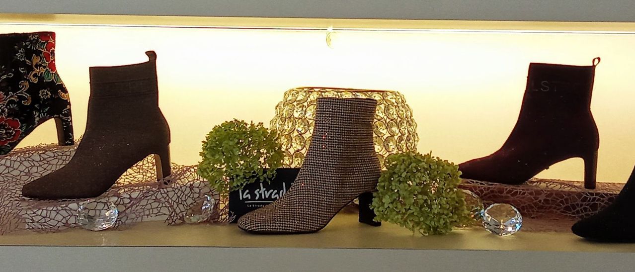 Ein brauner karierter Stiefel mit hohem Absatz wird auf einem Regal mit dekorativen Pflanzen und einer goldenen Lampe ausgestellt.