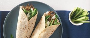 Zwei Lamm- und Linsen-Wraps mit Gurke und Minze auf einem blauen Teller, begleitet von einer kleinen Schüssel mit geschnittenen Gurken.