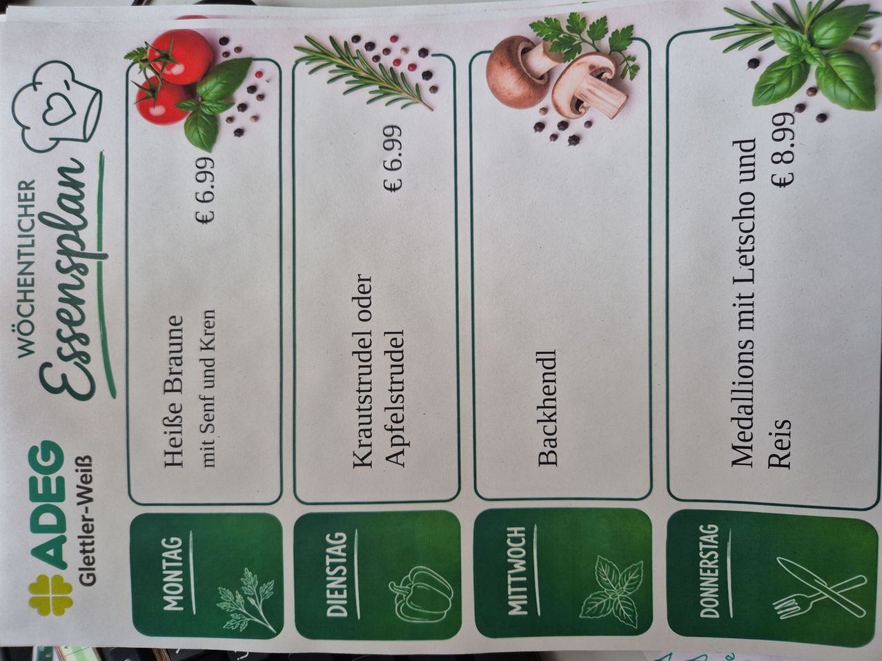 Ein Menü, das Preise und Zutaten für Mahlzeiten zeigt: Heiße Tomaten-Basilikum-Suppe, Krautstrudel oder Apfelstrudel, Backhendl. Jedes Element hat einen Preis, wobei einige auch zusätzliche Zutaten enthalten.