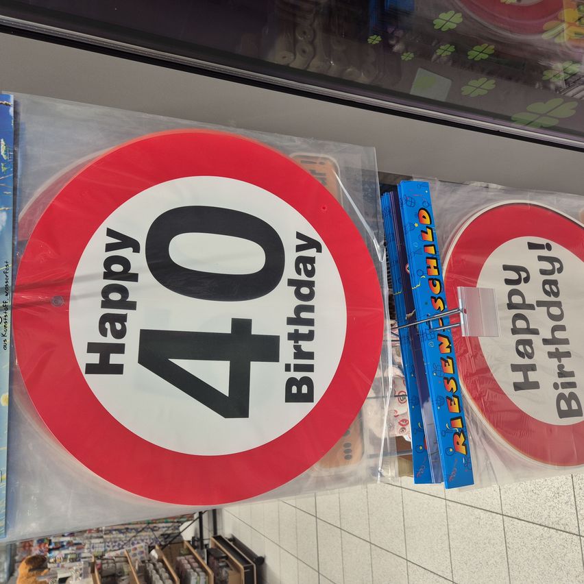 Two circular decorations with a red border and white background. The larger one has black text reading 'Happy 40th Birthday'. Next to it, a smaller one reads 'Happy Birthday'. Both are in plastic packaging.