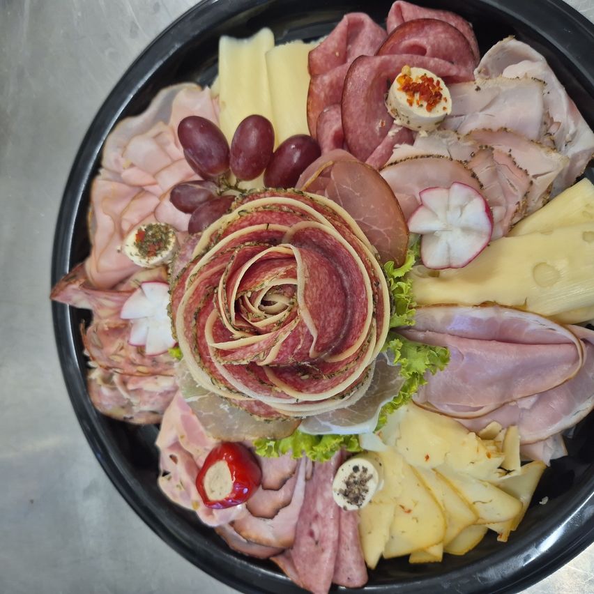 Eine Platte mit einer Auswahl an Fleisch, Käse und Trauben, kunstvoll arrangiert mit einem Zentrum aus geschnittenen Fleischscheiben, die eine Rose bilden.