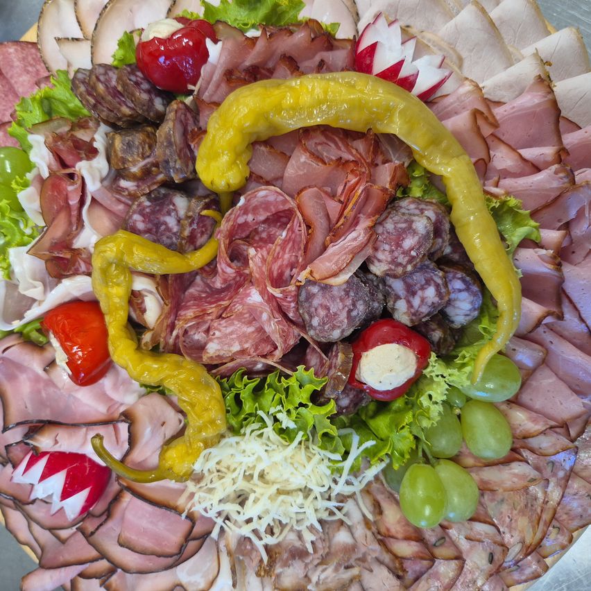 Ein Charcuterie-Brett zeigt eine Auswahl an gereiften Fleischsorten, darunter Salami, Prosciutto und Pepperoni. Es enthält auch Käse, Trauben und bunte Paprikaschoten.