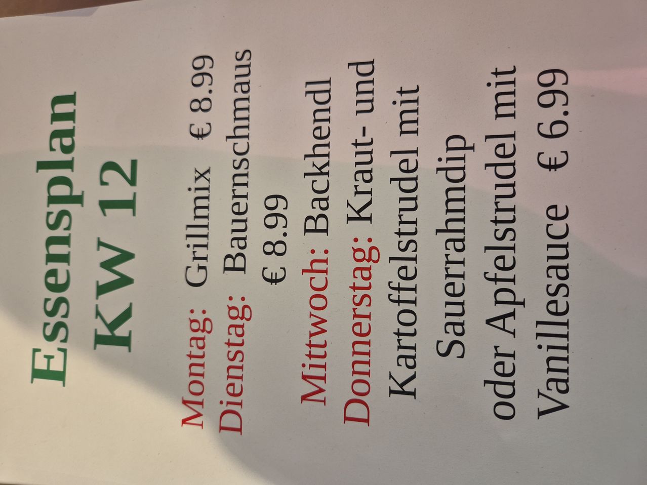 Ein Menüzettel eines Restaurants mit Preisen und Mahlzeitoptionen. Am Montag bietet es Grillmix für 8,99 €, Bauernschmaus für 8,99 € und Backend Kraut-und für 6,99 €. Am Dienstag bietet es Mittwöch für 8,99 €, Donnerstag für 6,99 € und Kartoffelstrudel mit für 6,99 €. Sauerrahmdip oder Apfelstrudel mit Vanillesauce.