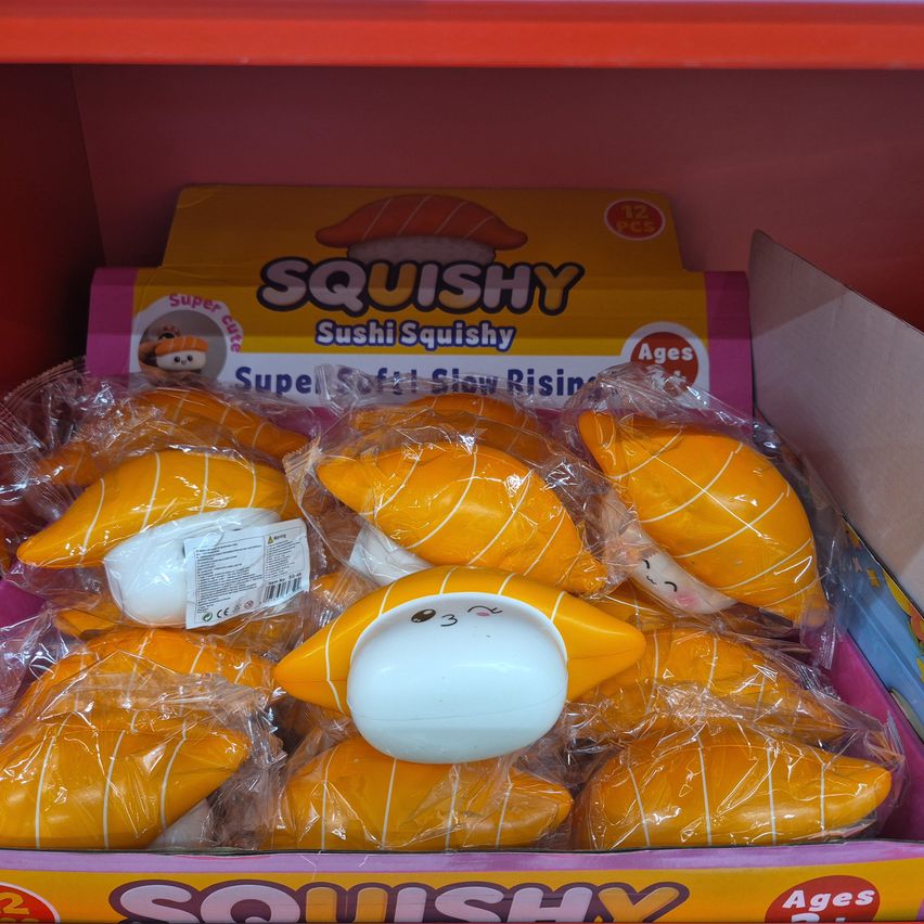 A box of Squishy Sushi Squishy toys, each wrapped in plastic, displayed on a shelf. The toys are yellow with white stripes and have cute faces.