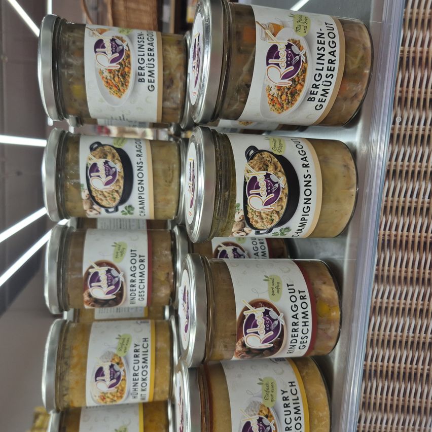 Stacked jars of various food items, each labeled with names like 'BERGLINSEN' and 'UNDERGBAOUT', and flavors such as 'GEMUSERAGOUT' and 'MERCURY', arranged in a transparent display case.