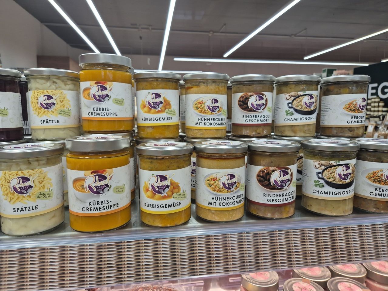 A display of assorted canned food products on a store shelf, including pumpkin soup and various curries. Each jar has a distinct label and color scheme, placed in rows for easy viewing.