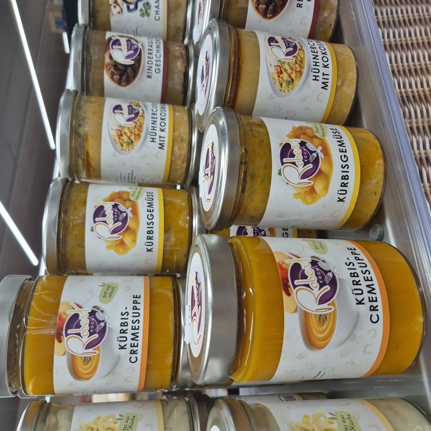 Multiple jars of food products are displayed in a store. The jars are labeled with various types of food, including pumpkin and curry. The jars are in a transparent container.
