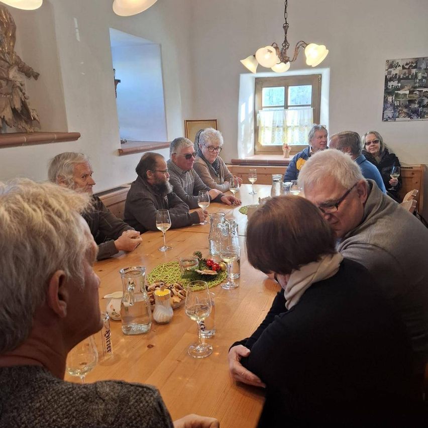 Gruppe von Menschen sitzt um einen Tisch herum, unterhält sich, mit Weingläsern und Essen.