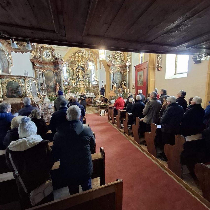 Ein Kircheninneres mit Gemeindemitgliedern auf Kirchenbänken, einem Altar vorne und religiösen Artefakten an den Wänden.