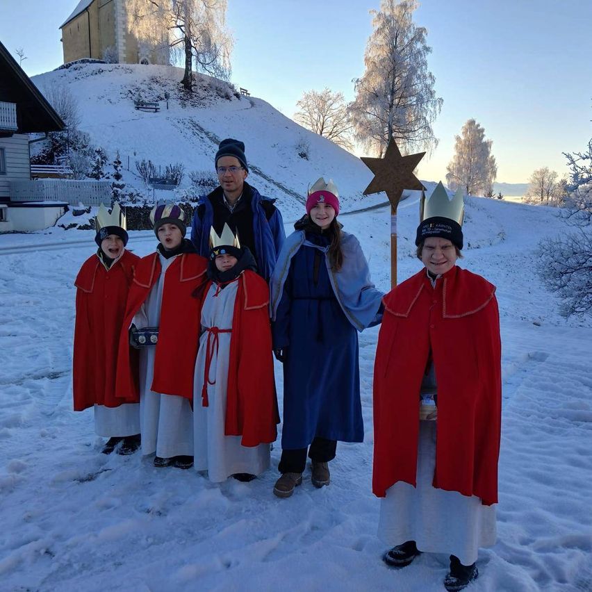 Eine Gruppe von Menschen in traditioneller Kleidung posiert für ein Foto im Schnee. Hinter ihnen steht ein Stern auf einem Stock.