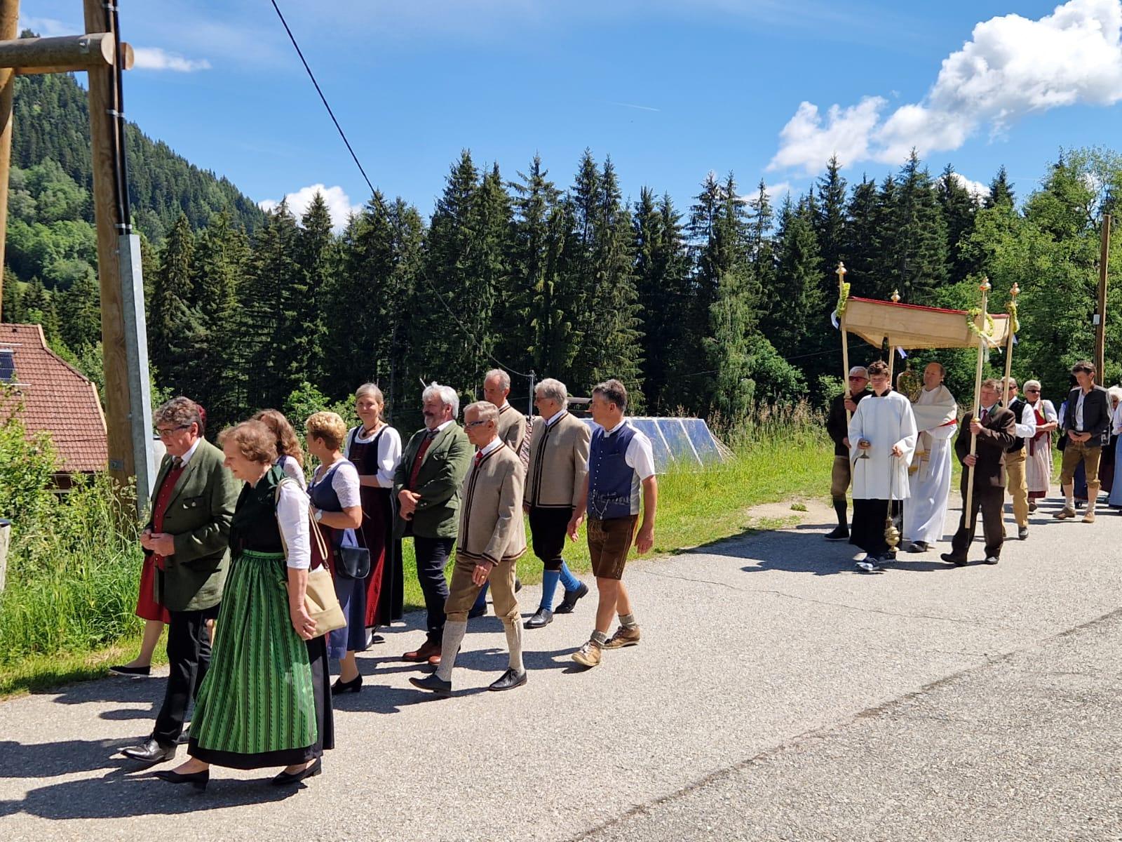 Prozession in Tracht mit Ministrant und Pfarrer in weißem Gewand vor Bergkulisse