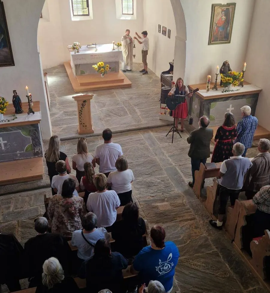 Eine Gruppe von Menschen versammelt sich in einer Kirche, eine Frau spielt Gitarre vor dem Altar. Zwei Priester stehen in der Nähe des Altars, und einige Kerzen sind angezündet.