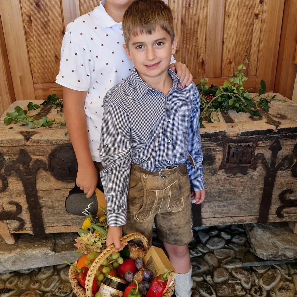 Zwei Jungen stehen vor einer Holztür. Ein Junge hält einen Korb mit Gemüse und Obst.