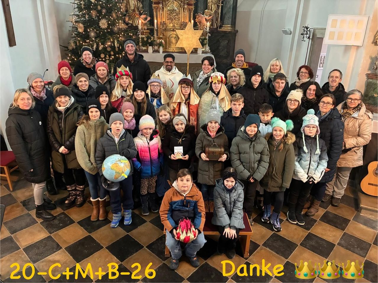 Eine Gruppenaufnahme von Erwachsenen und Kindern in Winterkleidung, vor dem Altar einer Kirche, mit einem Weihnachtsbaum und Stern im Hintergrund.