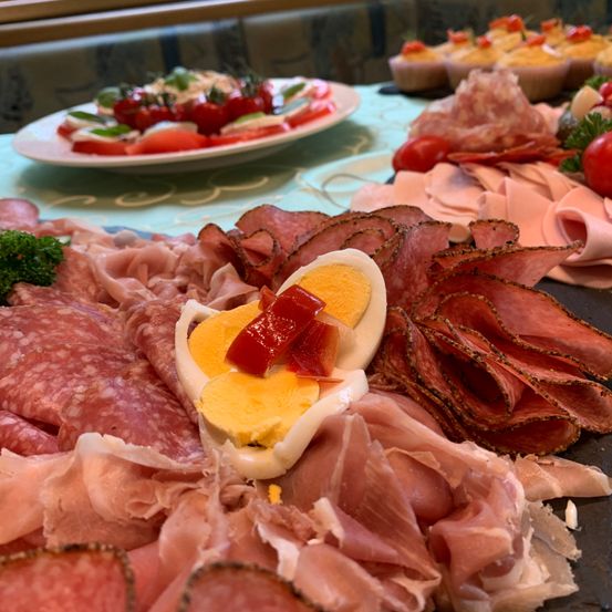Eine Charcuterie-Platte mit verschiedenen Fleischsorten, einem halbierten Ei mit roter Paprika und einer Platte mit Tomaten und Käse.
