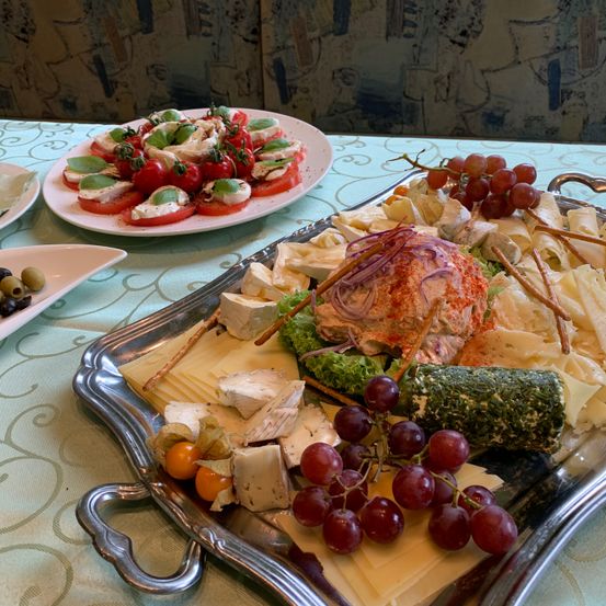 Ein silbernes Tablett mit einer Auswahl an Käse, Trauben und einer Tomatensalat auf einem Tisch.