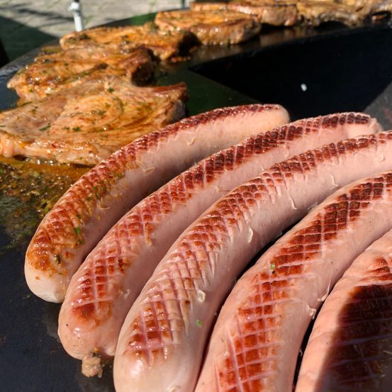 Nahaufnahme von gegrillten Würsten mit einem karierten Muster, neben einem gegrillten Steak auf einem Grillteller.