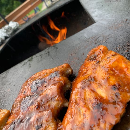 Gegrillte Hähnchenflügel mit glänzender Glasur, über offenem Feuer zubereitet, mit rauchigem Hintergrund.