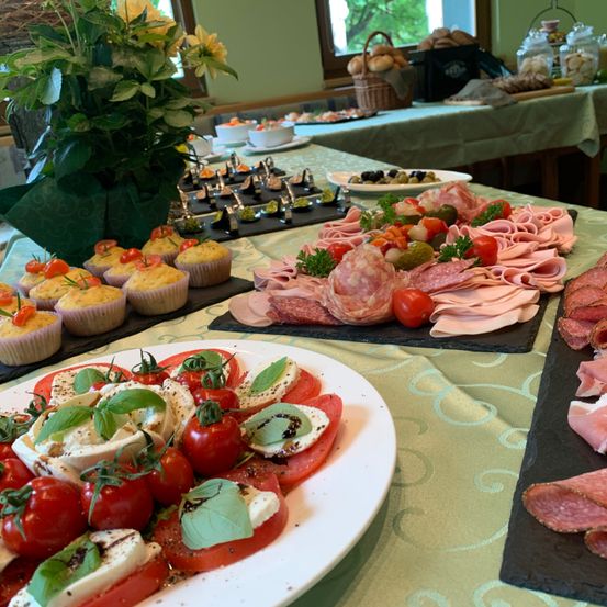 Ein Tisch mit verschiedenen Speisen, darunter eine Platte mit Fleisch, eine Scheibe mit Tomaten und Käse sowie Cupcakes mit Kirschtomaten obenauf.