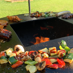Ein Grill mit verschiedenen Fleisch- und Gemüsesorten, darunter Würste, Rippchen und eine Mischung aus Paprika, Zucchini und Champignons, alles gewürzt und bereit zum Kochen.