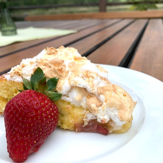 Ein Stück Zitronen-Baiser-Torte mit einer Erdbeere auf einem weißen Teller auf einem Holztisch.