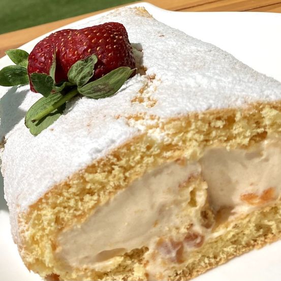 Ein Stück Kuchen mit einer Erdbeere obenauf, bestreut mit Puderzucker, zeigt seine cremige Füllung.