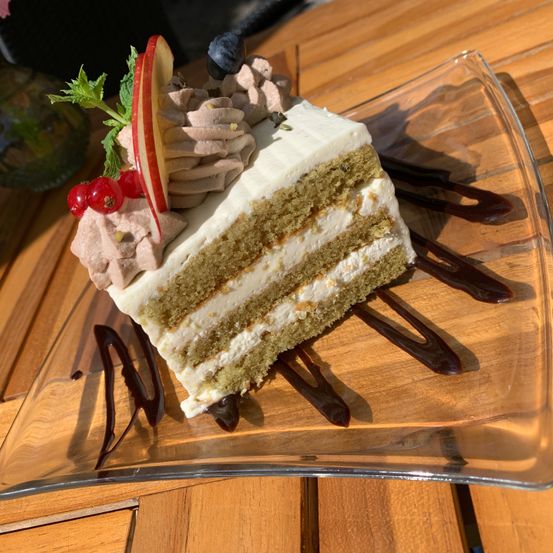 Ein Stück Kuchen mit weißer Glasur, einem Apfelstück und Schokoladenraspeln auf einem klaren Teller.