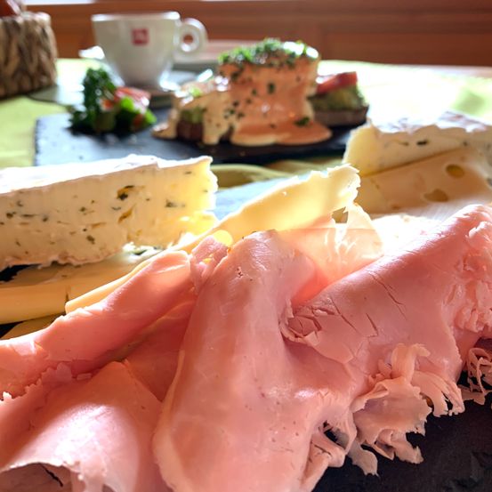 Ein Nahaufnahme einer Charcuterie-Platte mit verschiedenen Käsesorten, Fleisch und Garnierungen auf einem Tisch, mit einer Tasse Kaffee im Hintergrund.