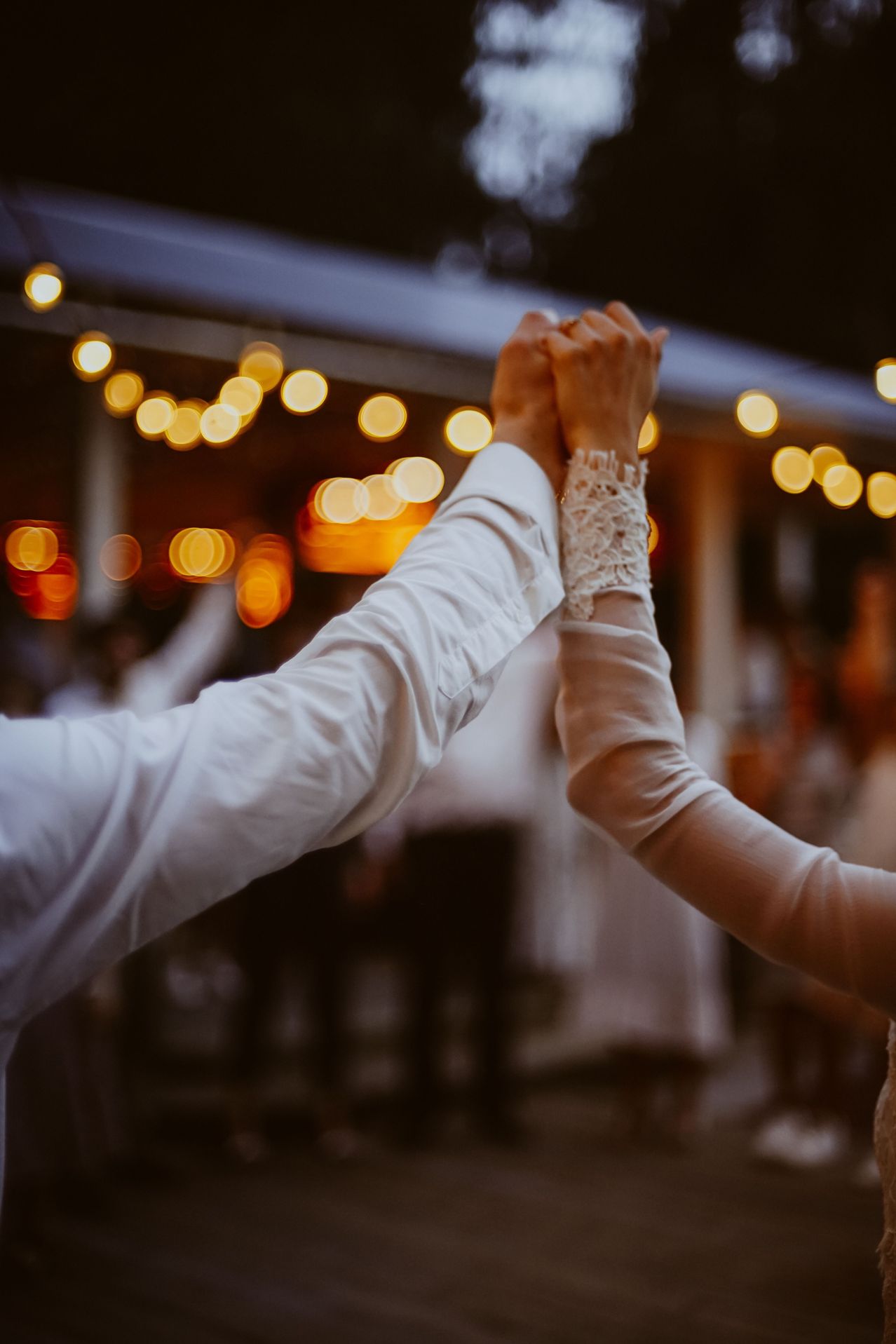 Ein Paar tanzt auf einer Hochzeit, Hände ineinander, mit Bokeh-Lichtern im Hintergrund.