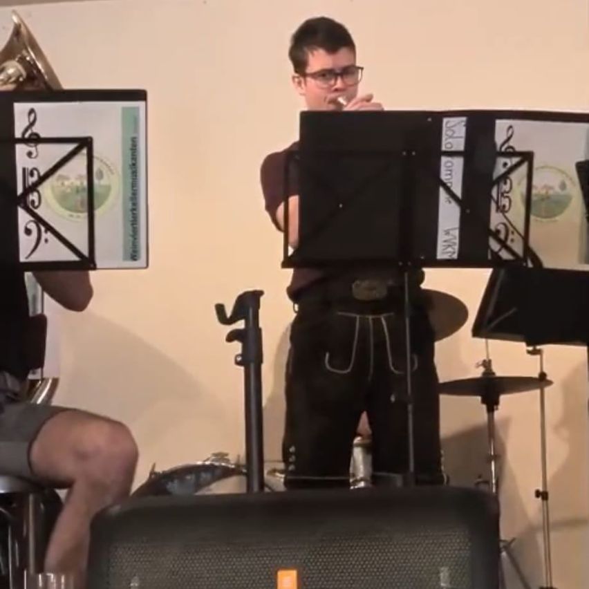 Two musicians are in a room. One plays a trumpet, and the other plays the flute. Music sheets are open in front of them.