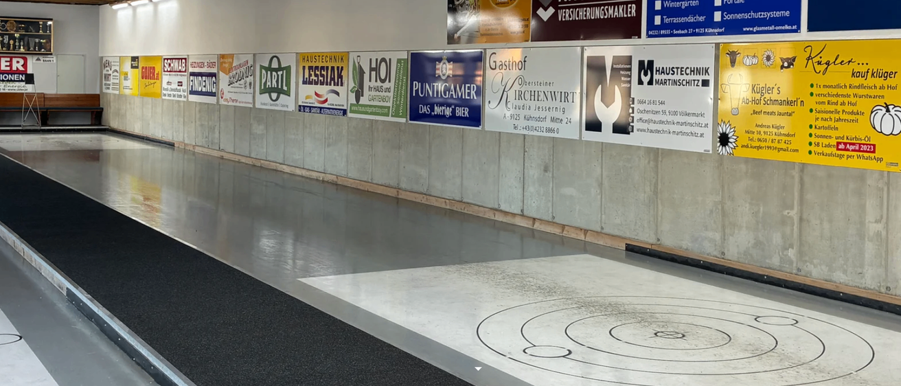 Ein Innenraum mit poliertem Boden hat mehrere Poster an der Wand, darunter Haustechnik Lessiak, Hoi Haus und Gartenboy und andere. Der Boden hat kreisförmige Markierungen.