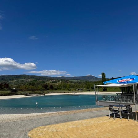 Ein Outdoor-Essbereich mit einem blauen Schirm steht in der Nähe eines großen Pools unter einem klaren Himmel mit Bergen im Hintergrund.
