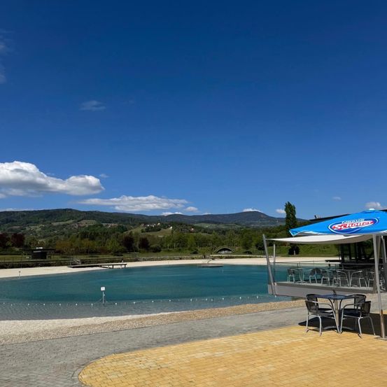 Ein Outdoor-Essbereich mit einem blauen Schirm steht in der Nähe eines großen Pools unter einem klaren Himmel mit Bergen im Hintergrund.