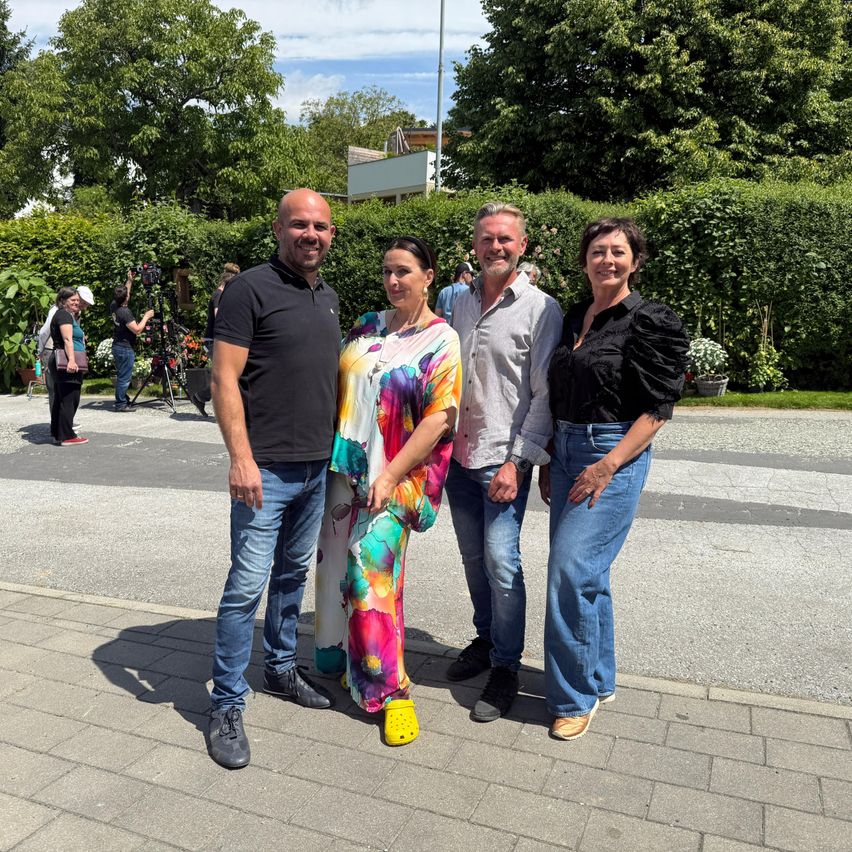 Vier Menschen posieren für ein Foto in einem Park, zwei Männer und zwei Frauen, mit Grün und Bäumen im Hintergrund.