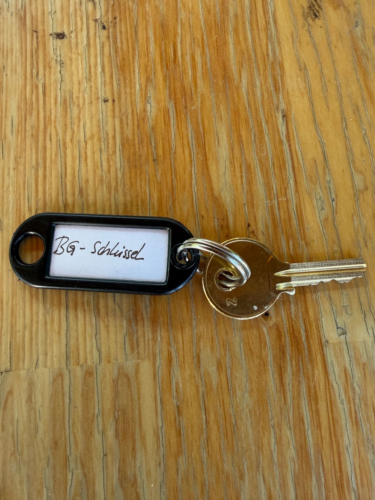 Ein Schlüssel mit einem schwarzen Etikett BG-sdlisse auf einer Holzoberfläche.