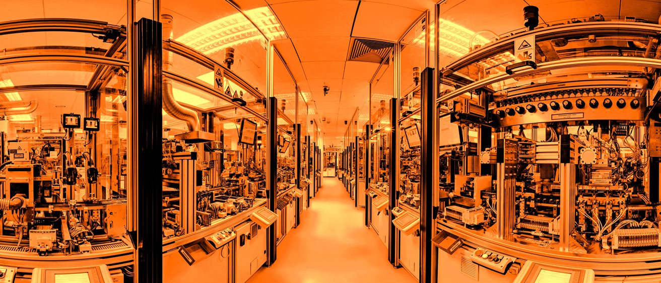 Ein langer Flur in einer Fabrik mit Glaswänden und mehreren Maschinen mit elektronischer Ausrüstung im Inneren.