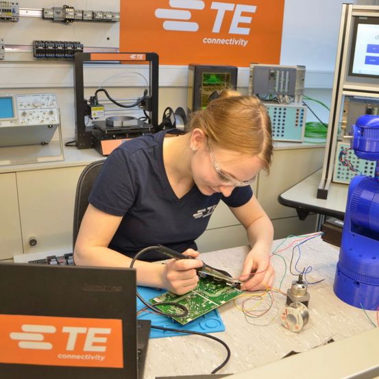 Eine Frau mit Brille arbeitet in einem Labor an einer Leiterplatte.