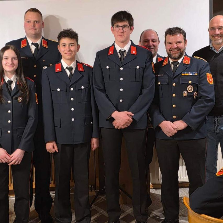 A group of uniformed individuals, likely firefighters, are posing for a photo. They stand in two rows, with three people in the front and four in the back. They wear similar uniforms with red and gold insignias.