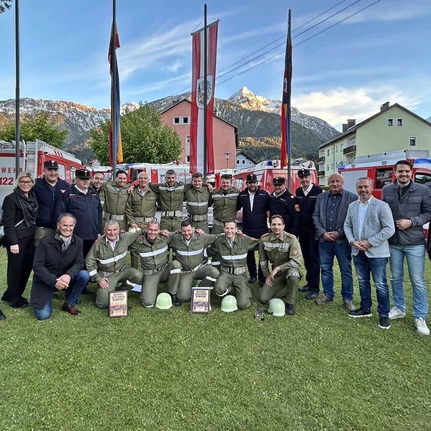 Eine Gruppe von Feuerwehrleuten und Beamten posiert vor einem Berg in Uniformen und hält Plaketten.