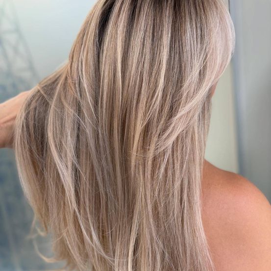 Eine Nahaufnahme einer Frau mit langen, hellbraunen Haaren, die in sanften Wellen gestylt sind, von hinten betrachtet, mit einem unscharfen Hintergrund.