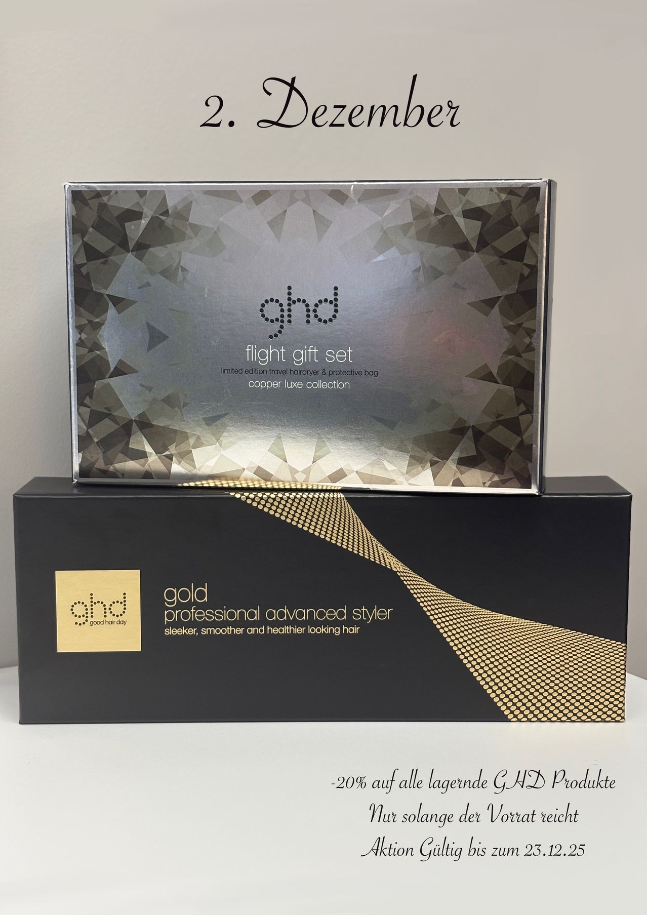 Eine silbergraue Metallbox mit 'ghd flight gift set' darauf, gestapelt auf einer schwarzen Box mit goldenen Akzenten.