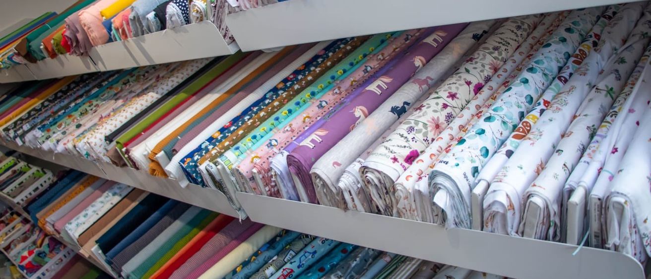 Ein weißer Regal mit verschiedenen Rollen farbiger, gemusterter Stoffrollen, einschließlich Blumen-, Einhorn- und Cartoon-Designs.